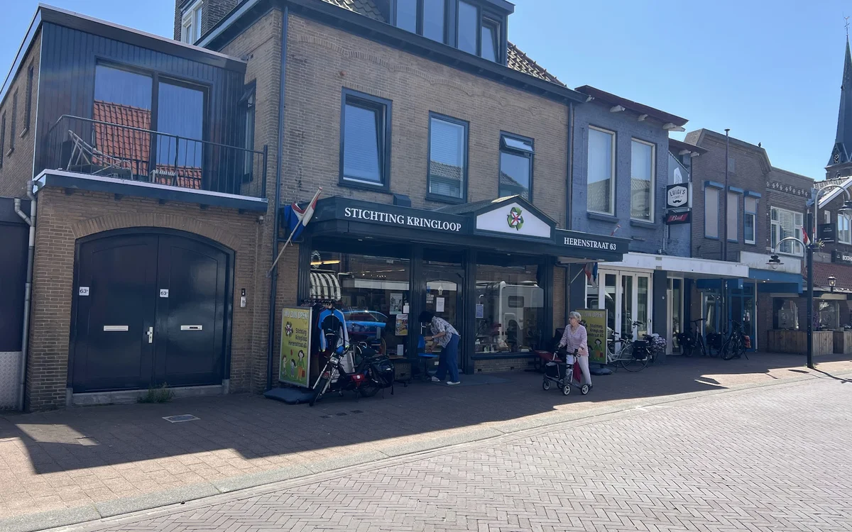 Voorgevel van kringloopwinkel met blauwe luifel, etalages en ingang aan Herenstraat