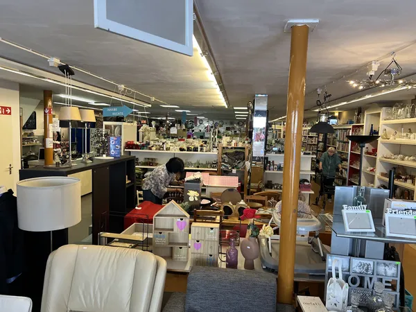 Winkelinterieur met stellingen, toonbanken en diverse spullen; een persoon werkt achter in de winkel