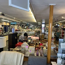 Winkelinterieur met stellingen, toonbanken en diverse spullen; een persoon werkt achter in de winkel