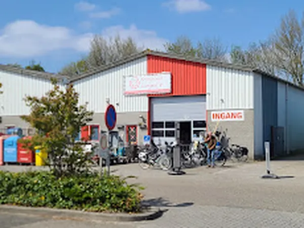 Grijswit pand met rood accenten en grote laaddeuren, fietsen geparkeerd ervoor, winkelvoorgevel overdag