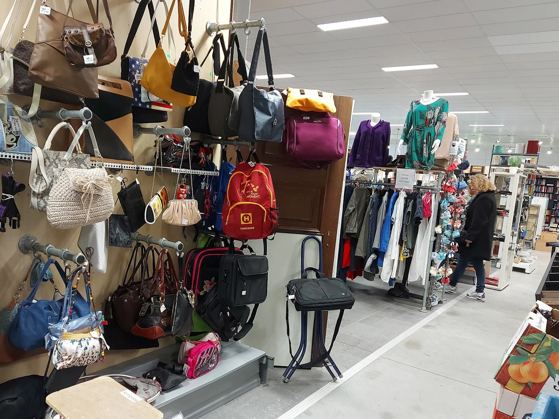 Uitgestalde tassen, rugzakken en kledingrekken in een kringloopwinkel
