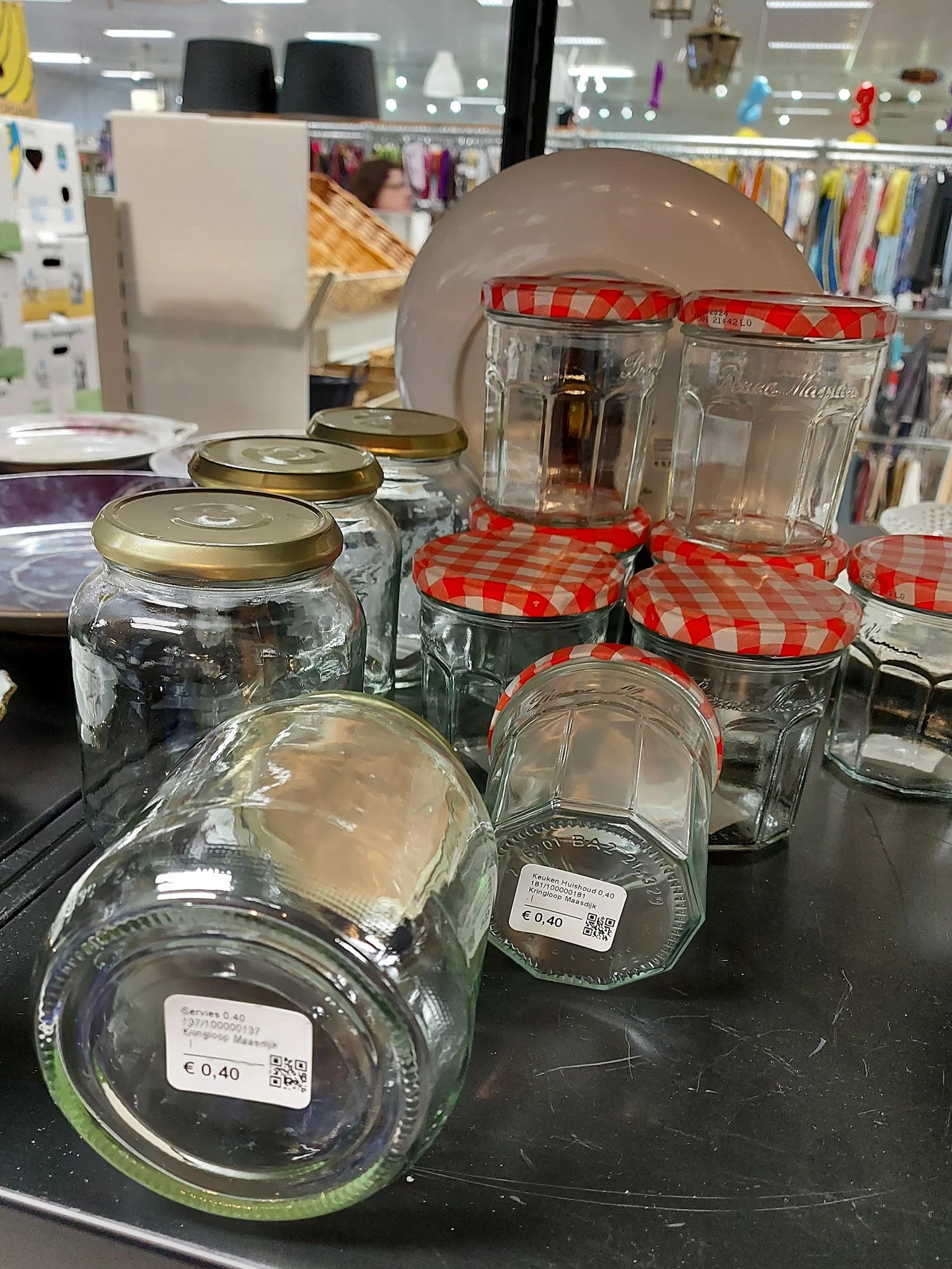 Glazen potten en bokalen met metalen en rood-witte geruite deksels op een zwarte tafel
