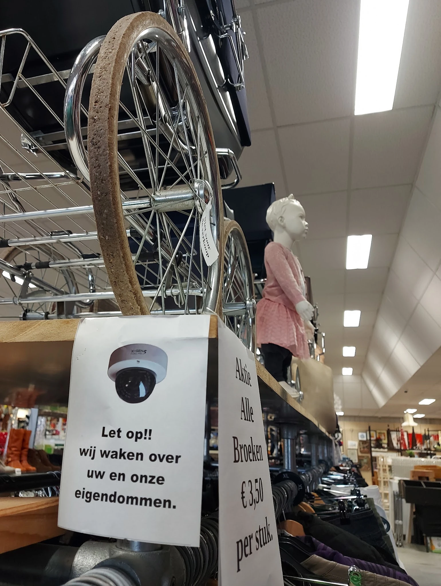 Winkelinterieur met fietsen aan een rek, etalagepop in roze jurk, en plafondverlichting