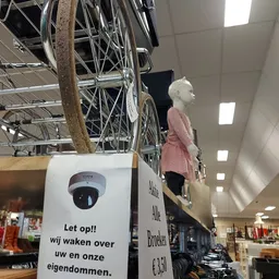 Winkelinterieur met fietsen aan een rek, etalagepop in roze jurk, en plafondverlichting