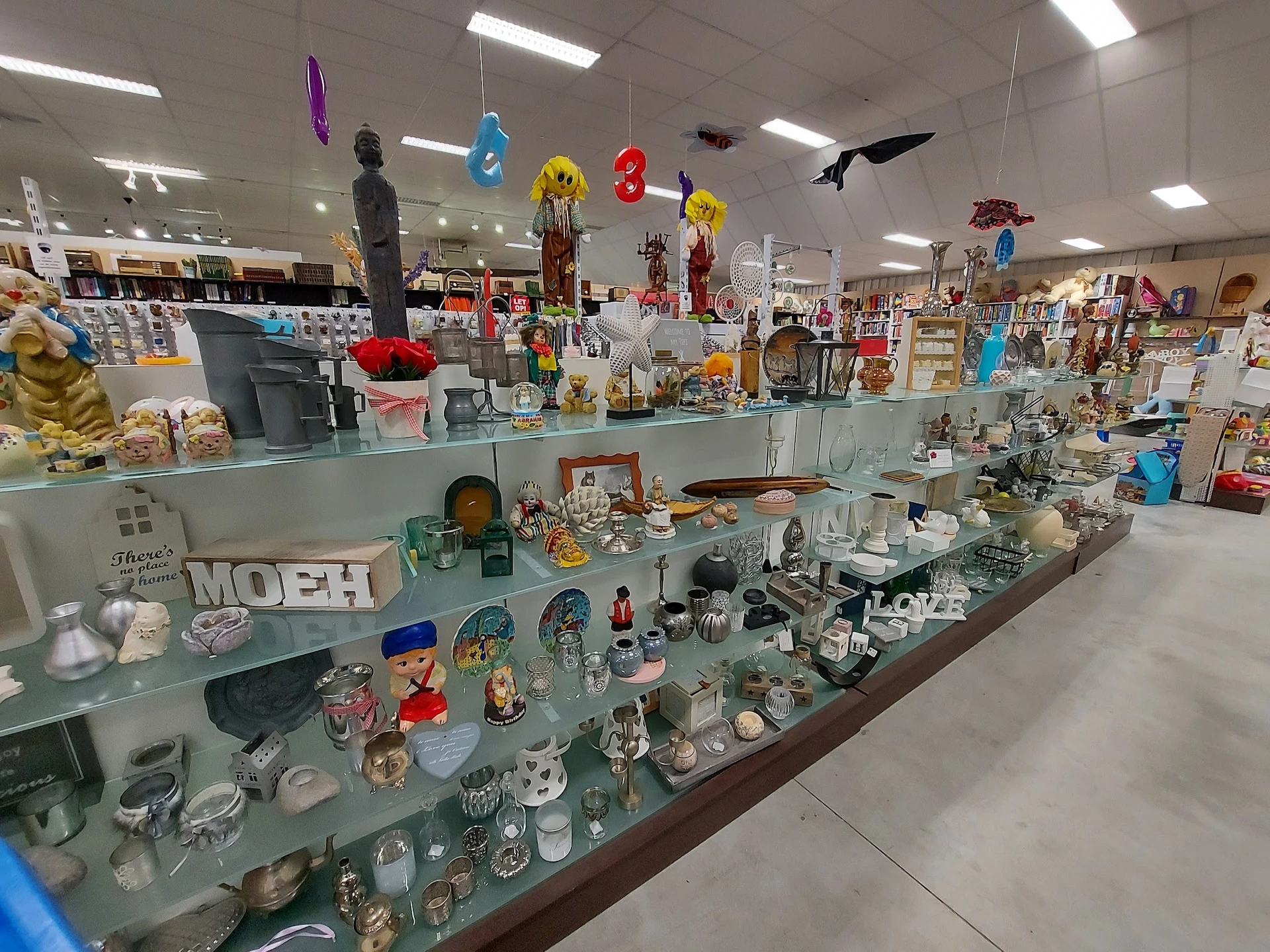 Glazen vitrinekast met diverse huishoudelijke artikelen, serviesgoed, figuren en decoratieve items in een kringloopwinkel