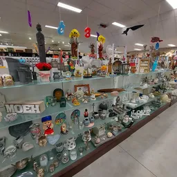 Glazen vitrinekast met diverse huishoudelijke artikelen, serviesgoed, figuren en decoratieve items in een kringloopwinkel