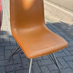 Oranje lederen stoel met zwart metalen frame op een terras.