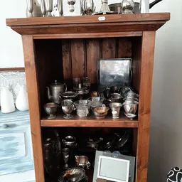 Houten kastje met twee planken vol met zilveren en zwarte serviesgoed, kopjes, kannen en andere huishoudelijke artikelen