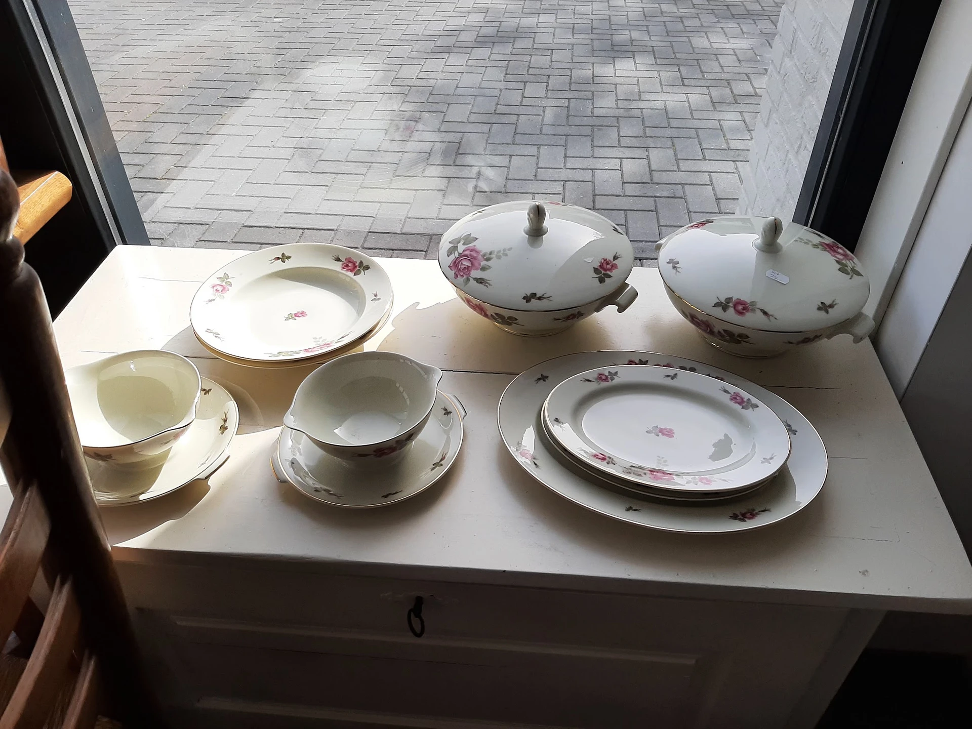 Servies met bloemmotief: borden, schalen, kopjes en schotels op wit dressoir