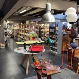 Winkelvloer met diverse meubels, lamp, tafel en stellingen vol spullen tegen de wanden