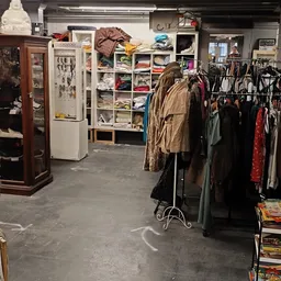 Rekken met tweedehands kleding, waaronder jassen en jurken, in de winkelruimte