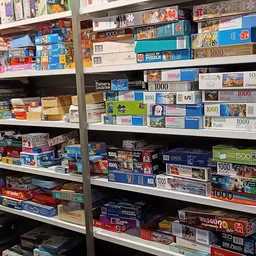 Volle stellingen met puzzels in dozen, waaronder veel 1000-stukspuzzels van verschillende merken