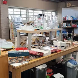 Kringloopwinkelrek met huishoudelijke spullen zoals glazen, serviesgoed, boeken en diverse gebruiksartikelen.