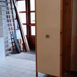 Hal of gang met deuropening, witte muur en houten deur, met stellingen zichtbaar op achtergrond