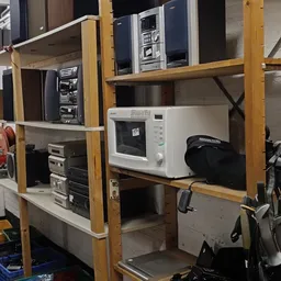 Houten stellingen met elektronische apparaten zoals een magnetron, versterker en andere huishoudelijke items