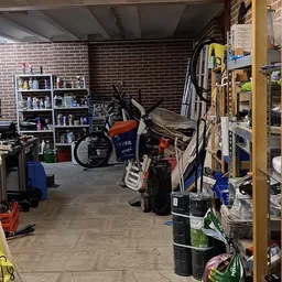 Werkplaats met fietsen, gereedschap, stellingen met onderdelen en materialen tegen bakstenen muur