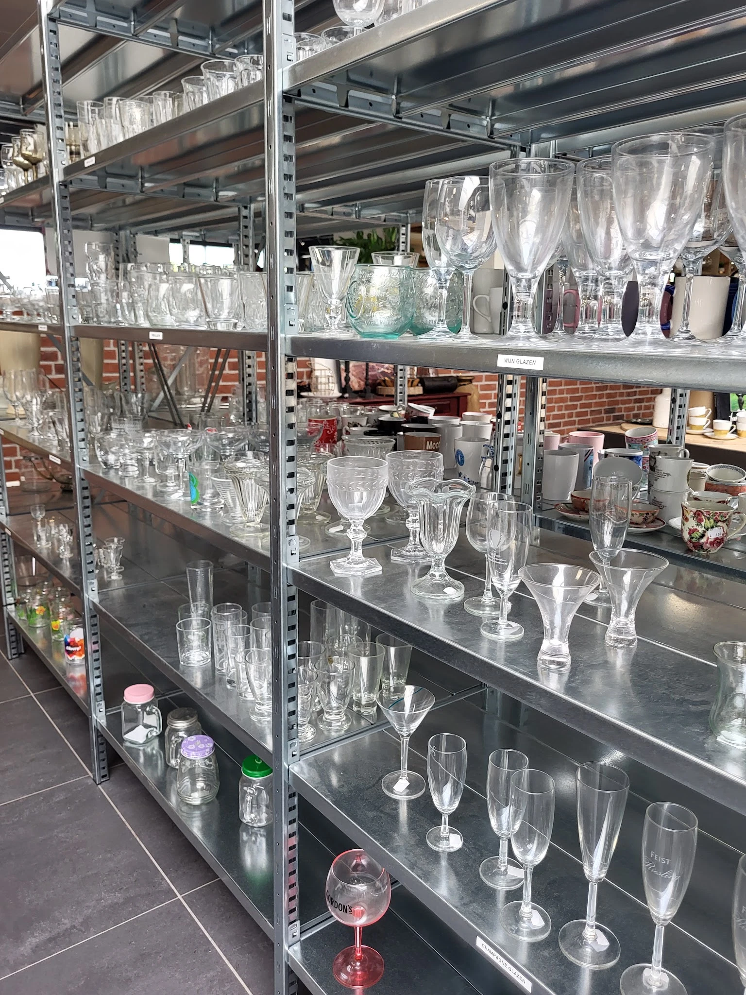 Stellingen met diverse glazen en kristallen serviezen, waaronder wijnglazen, bekers en vazen.