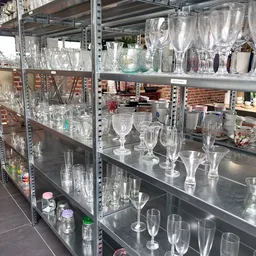 Stellingen met diverse glazen en kristallen serviezen, waaronder wijnglazen, bekers en vazen.