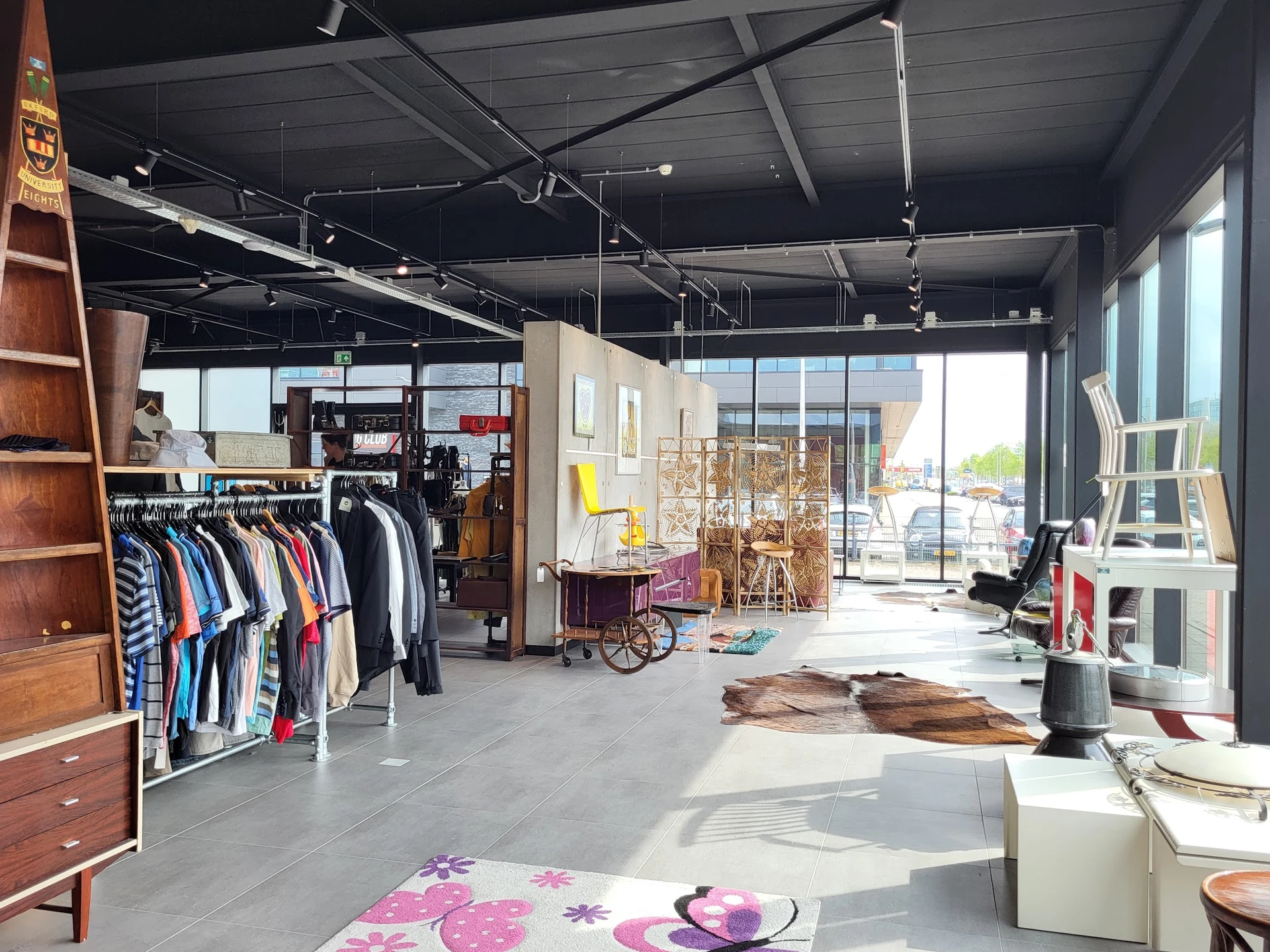 Spacious thrift store interior with clothing racks, furniture, vintage items and large windows with daylight