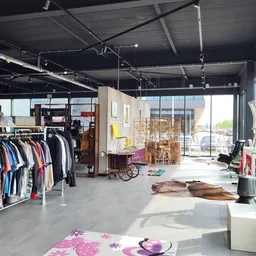 Spacious thrift store interior with clothing racks, furniture, vintage items and large windows with daylight