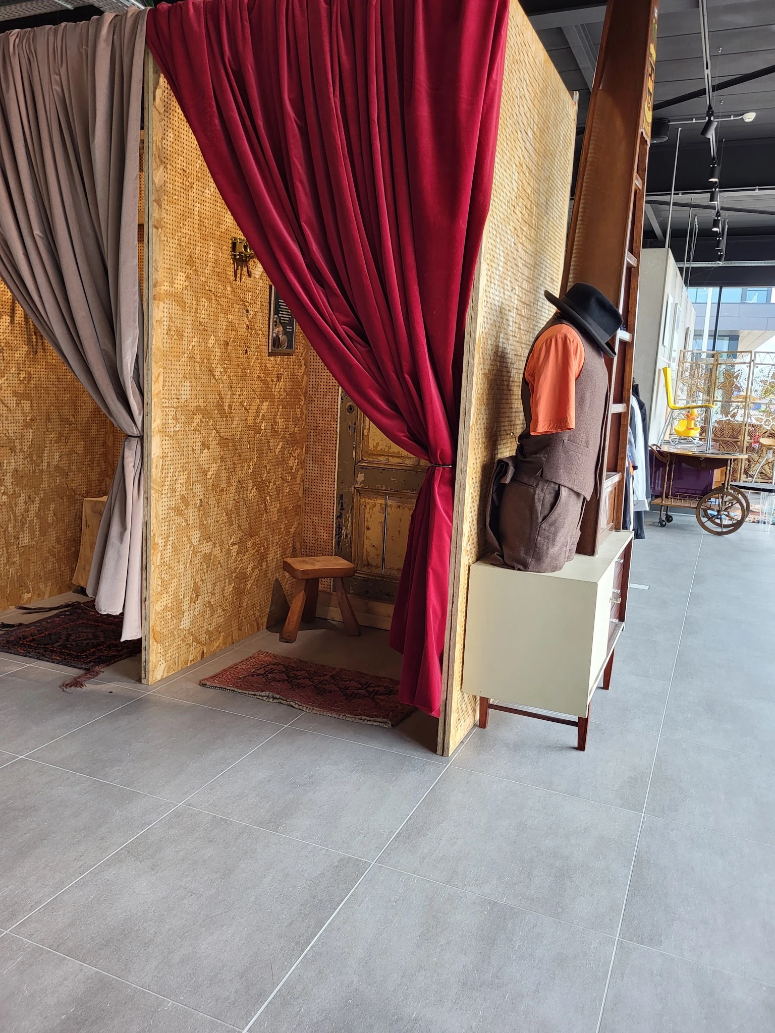 Winkelinterieur met kledingrekken, paskamers met gekleurde gordijnen en een hoedenmanchet op display.