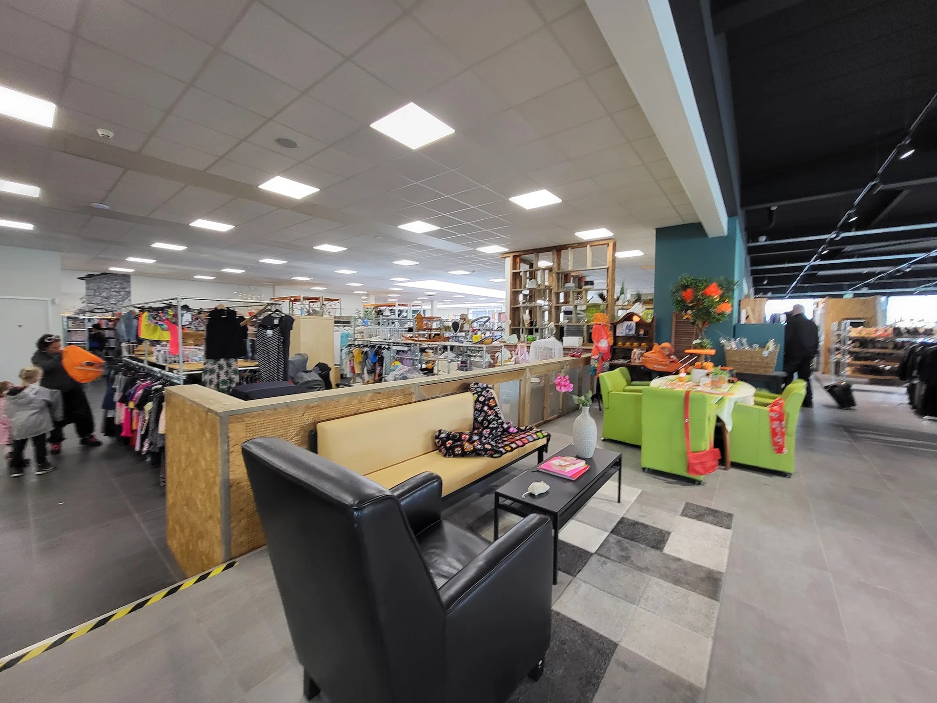 Winkelvloer van kringloopwinkel met zithoek, kledingrekken, stellingen en diverse spullen, heldere verlichting