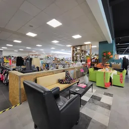 Winkelvloer van kringloopwinkel met zithoek, kledingrekken, stellingen en diverse spullen, heldere verlichting