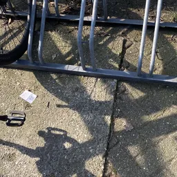 Metalen rek met schaduwen op asfalt, enkele kleine objecten zichtbaar