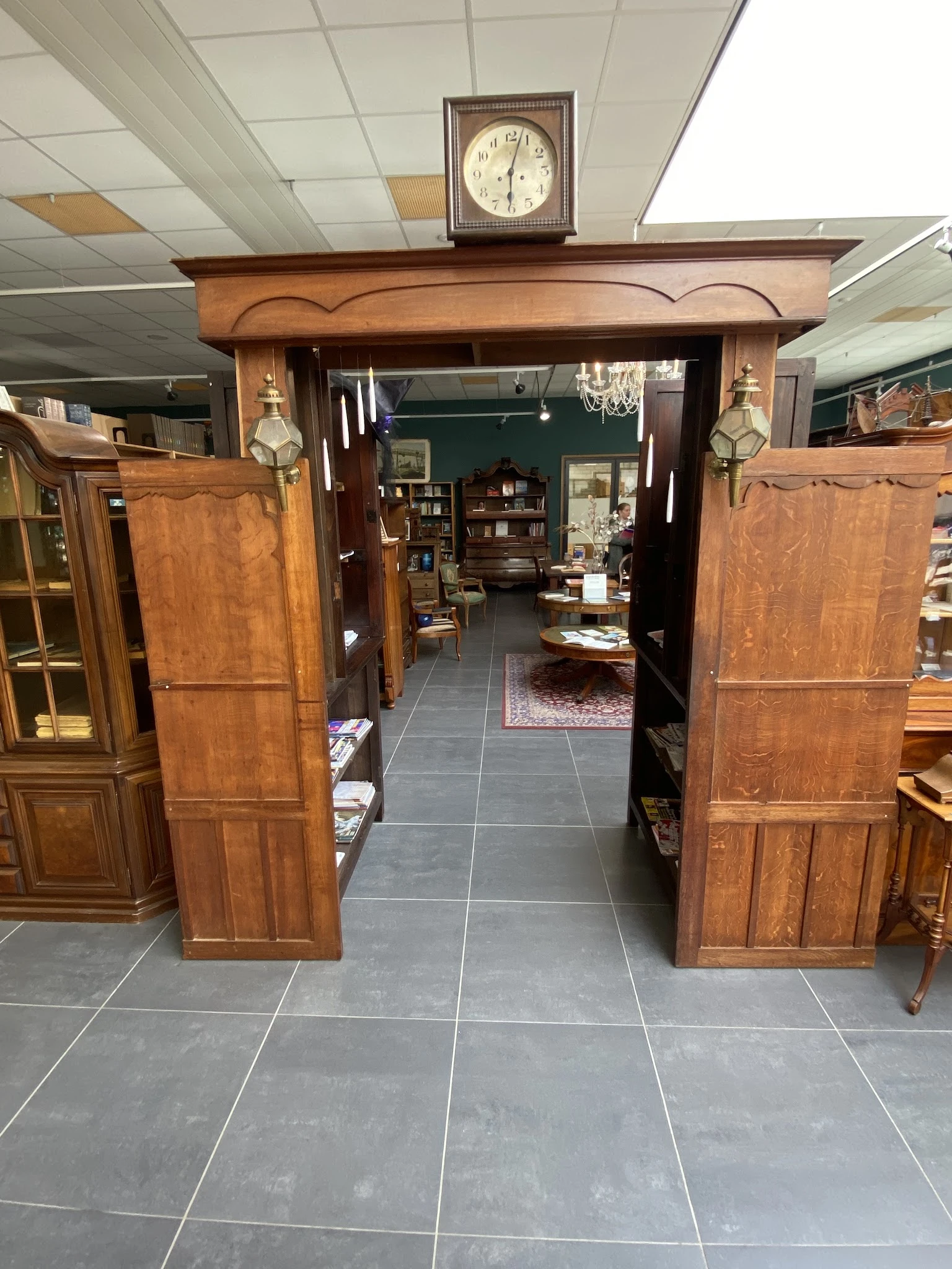 Zicht door houten deuren in een inrichting met donkergroene muur, kasten en meubels