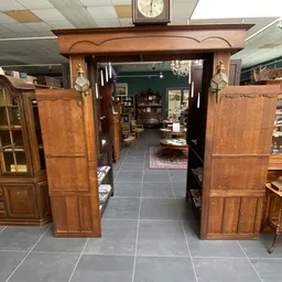Zicht door houten deuren in een inrichting met donkergroene muur, kasten en meubels