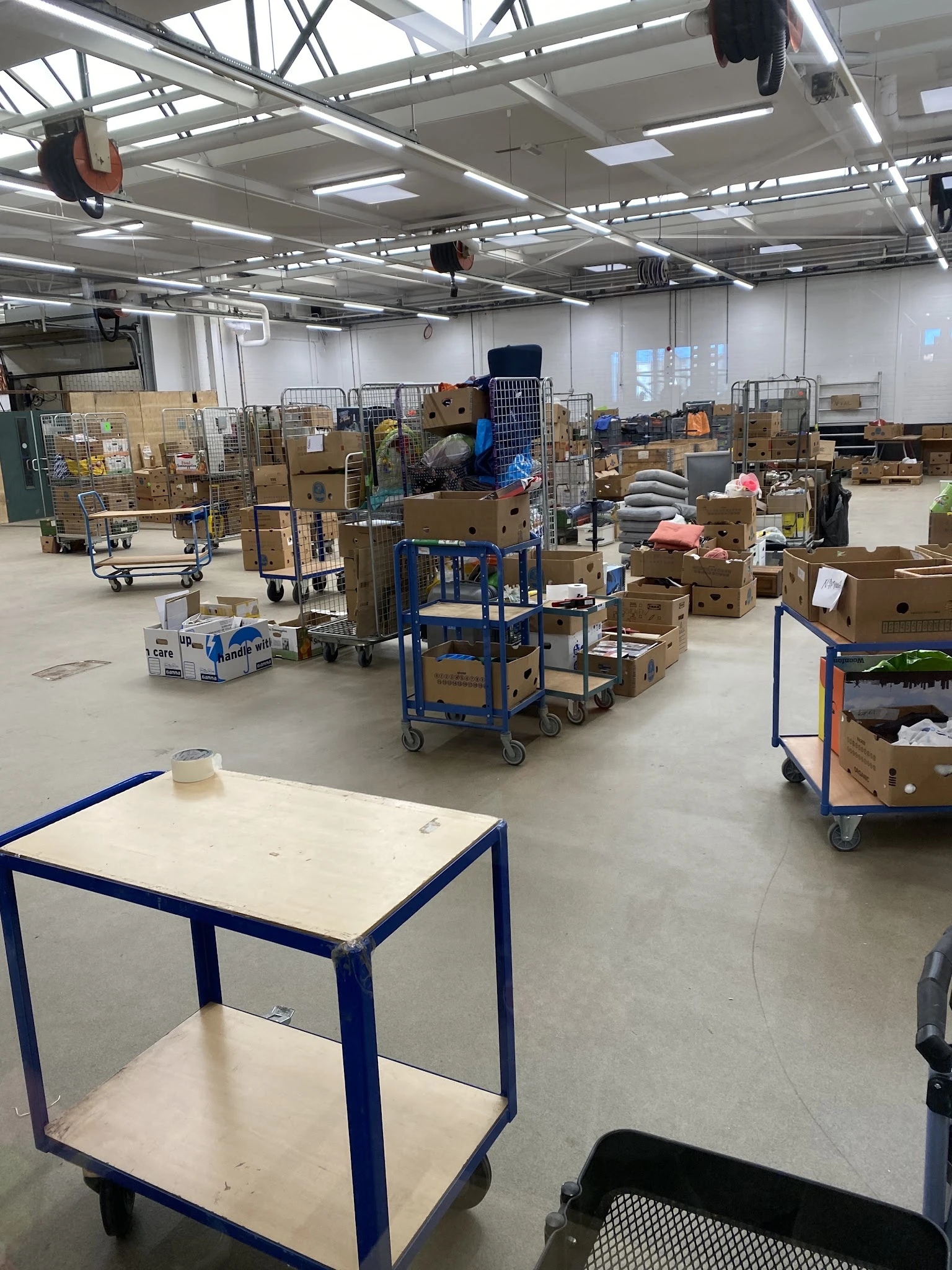Magazijnruimte met kartonnen dozen, stellingen en blauwe transportwagentjes vol spullen