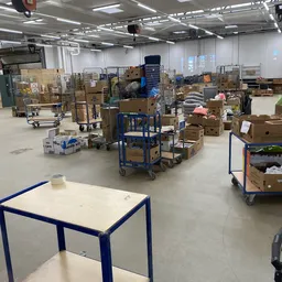 Magazijnruimte met kartonnen dozen, stellingen en blauwe transportwagentjes vol spullen