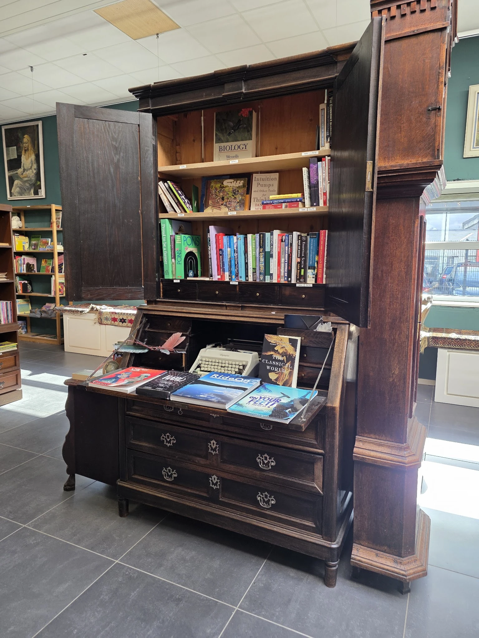 Donker houten bureau met boeken, typewriter en diverse spullen op het blad; boekenkasten erachter