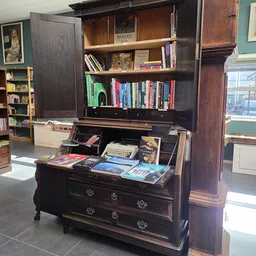 Donker houten bureau met boeken, typewriter en diverse spullen op het blad; boekenkasten erachter