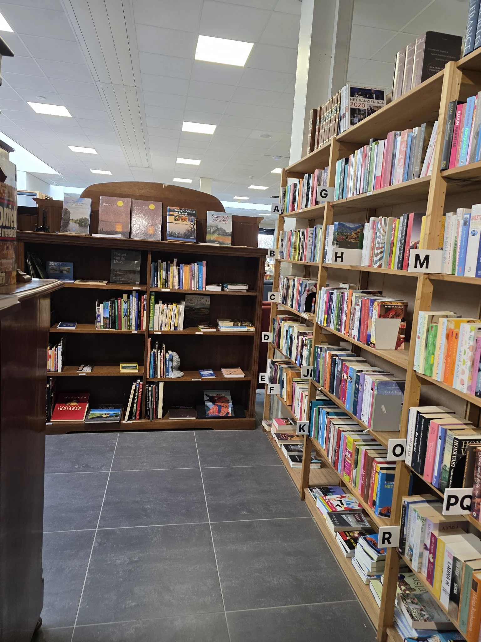 Boekenrekken in een kringloopwinkel met donkerbruine stellingen links en lichte houten kasten rechts, alfabetisch geordend