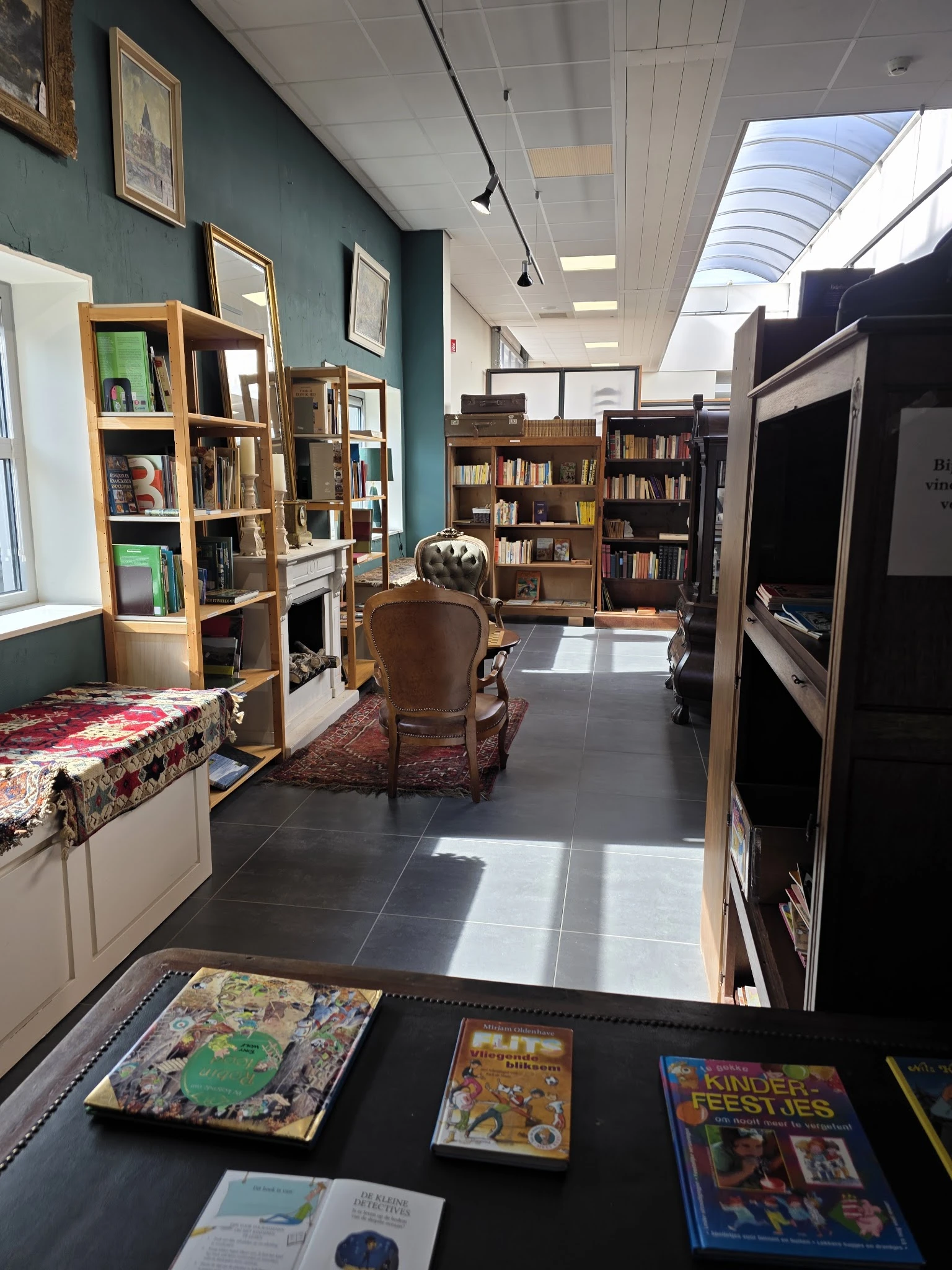 Leesruimte in kringloopwinkel met boekenkasten, een bruine stoel en een bank met kleed