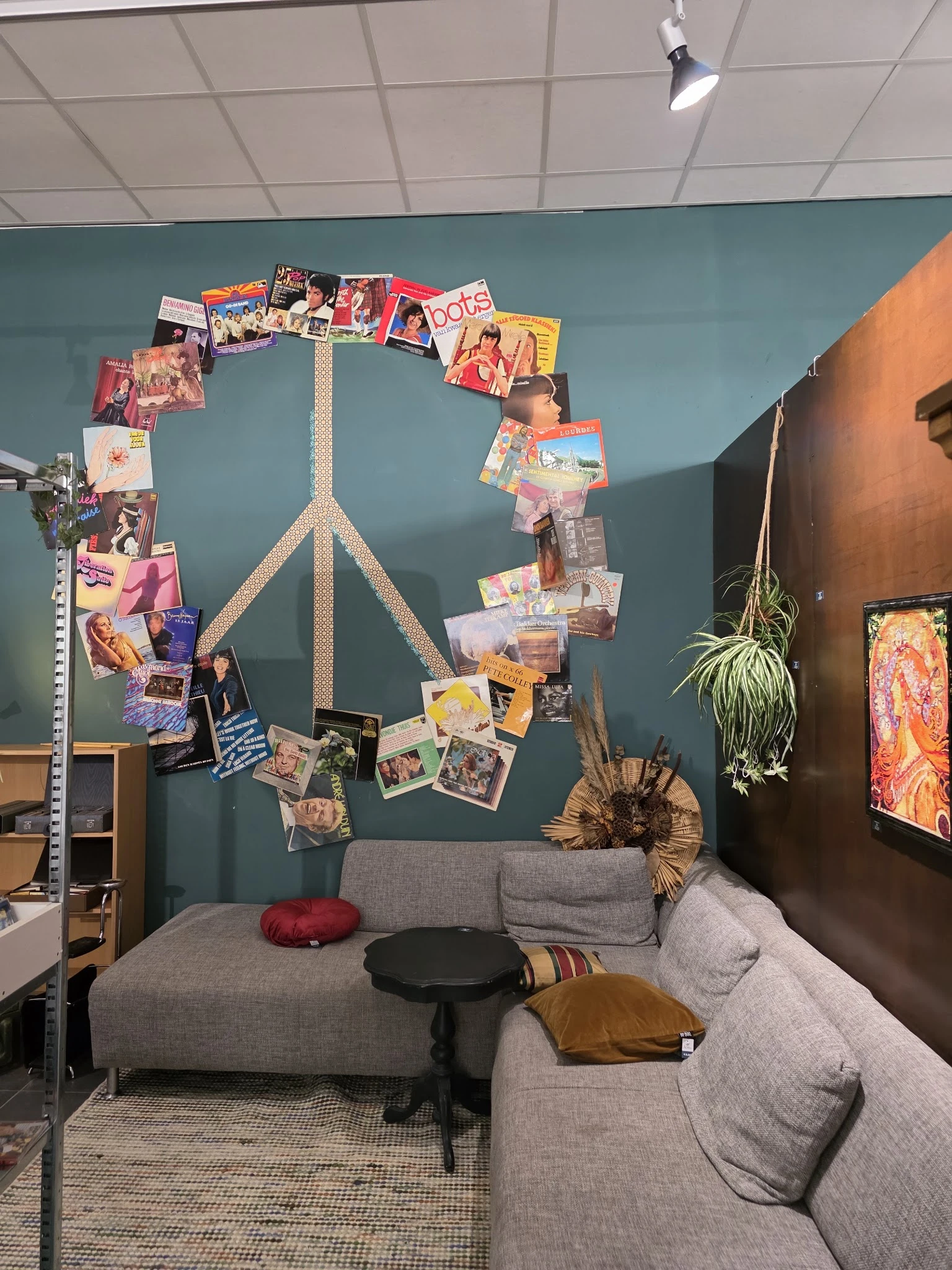 Slaapkamer ingericht met grijze bank, wanddecoratie met vredesteken van foto's en hangplanten tegen blauwgrijze en bruine muu