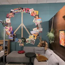 Slaapkamer ingericht met grijze bank, wanddecoratie met vredesteken van foto's en hangplanten tegen blauwgrijze en bruine muu