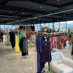 Rekken met tweedehands dameskleding in verschillende kleuren en stijlen in een ruime winkelruimte