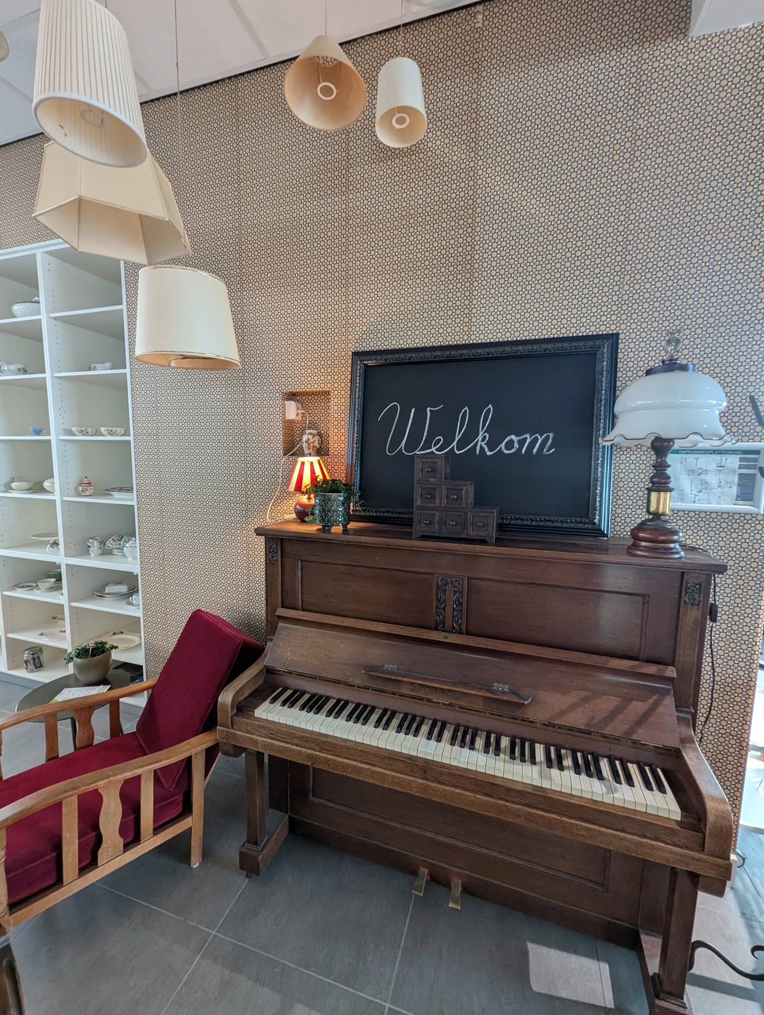 Bruine houten piano met zwart bord waarop 'Welkom' geschreven staat, met decoratieve items erop
