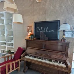 Bruine houten piano met zwart bord waarop 'Welkom' geschreven staat, met decoratieve items erop