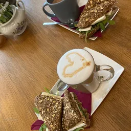 Cappuccino met latte art en belegde broodjes op houten tafel in lunchroom