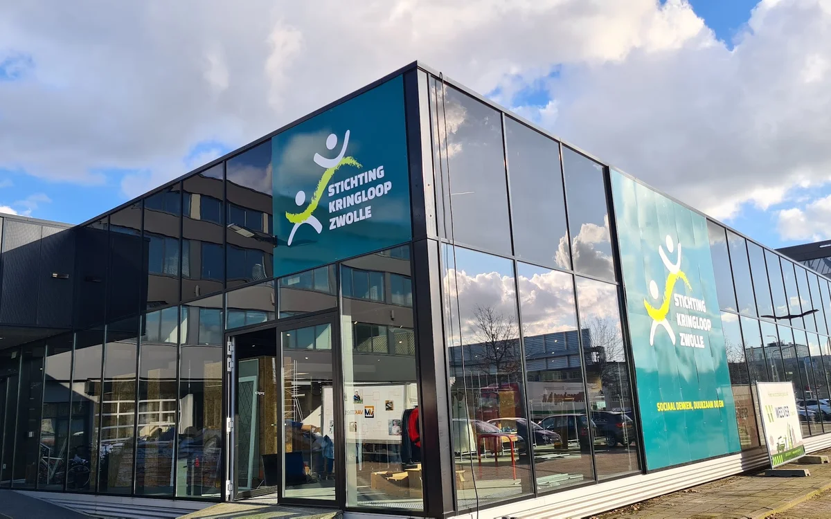 Moderne gevel van kringloopwinkel met grote glazen puien en blauwe logo-panelen
