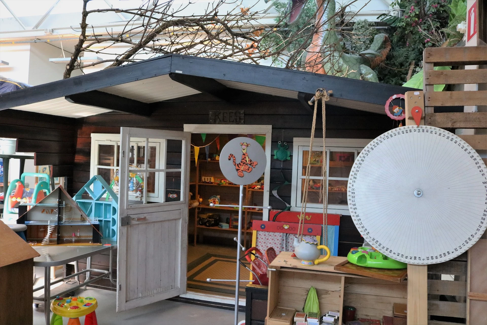 Uitstallingen met speelgoed en kinderspullen buiten de kringloopwinkel, waaronder een grote meetlint en diverse speelgoedarti