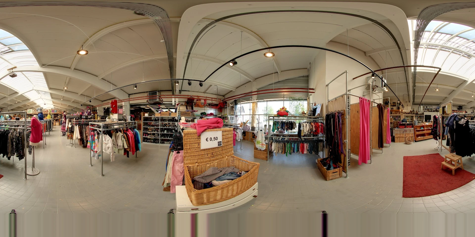 Winkelvloer van kringloopwinkel met kledingrekken, stellingen en een rieten mand met prijskaartje