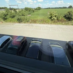 Parkeerplaats met enkele auto's, landbouwvelden op de achtergrond