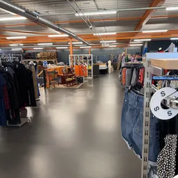 Ruim winkelinterieur met kledingrekken, oranje hefbruggen en diverse tweedehands kledingstukken uitgestald