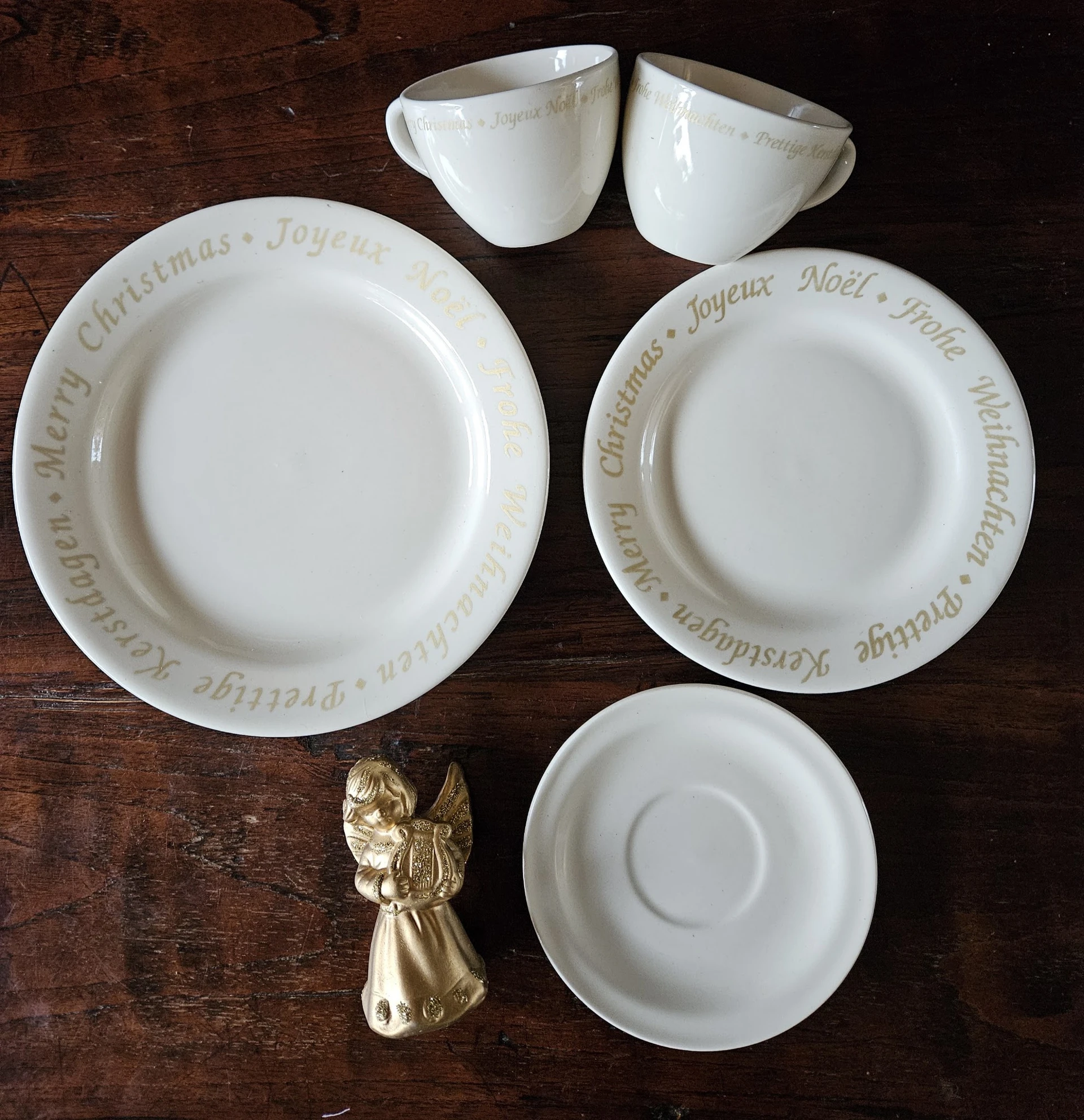 Wit servies met kerstopdruk: twee borden, schotel en gouden engelfiguur op houten tafel