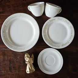 Wit servies met kerstopdruk: twee borden, schotel en gouden engelfiguur op houten tafel