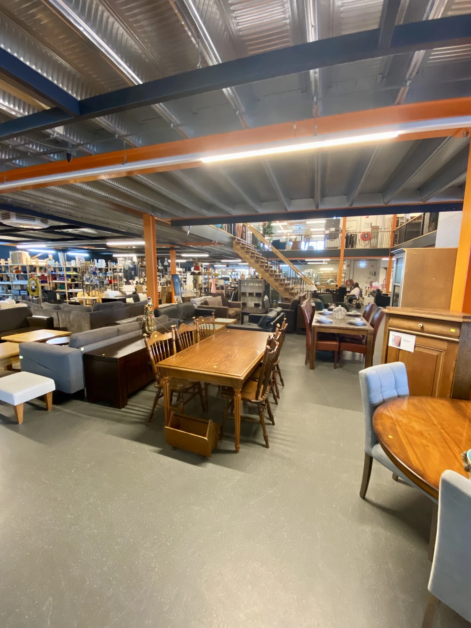 Winkelvloer met diverse meubelen en huishoudartikelen, waaronder houten tafels, stoelen, kasten en zitmeubels.